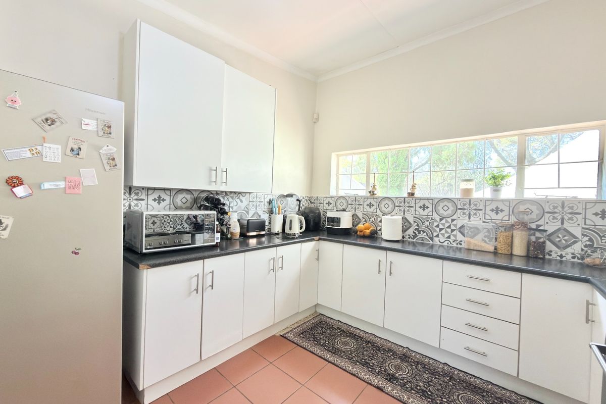 A functional kitchen featuring white cabinetry, dark laminate countertops, a decorative patterned tile backsplash, and tiled flooring with natural light from a horizontal window.