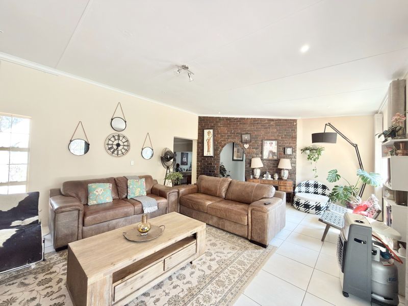 Spacious living room featuring an exposed brick accent wall, arched doorway, and neutral tiled flooring, offering a comfortable and inviting atmosphere.