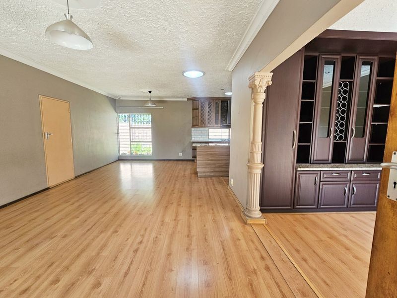 Spacious open-plan living area featuring laminate flooring, a decorative column, built-in cabinetry, and natural light from a skylight and window.