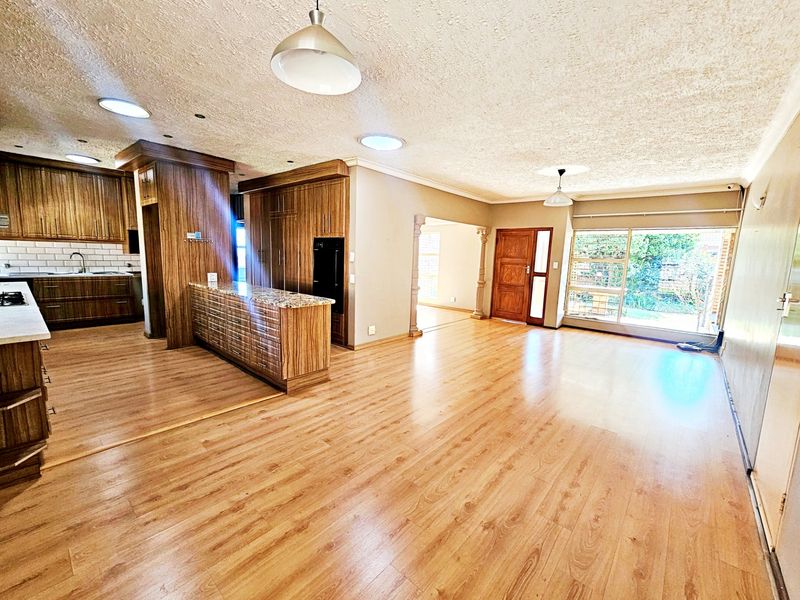 Spacious open-plan living and kitchen area featuring laminate flooring, modern wood-finish cabinetry, granite countertops, and abundant natural light through large sliding doors.