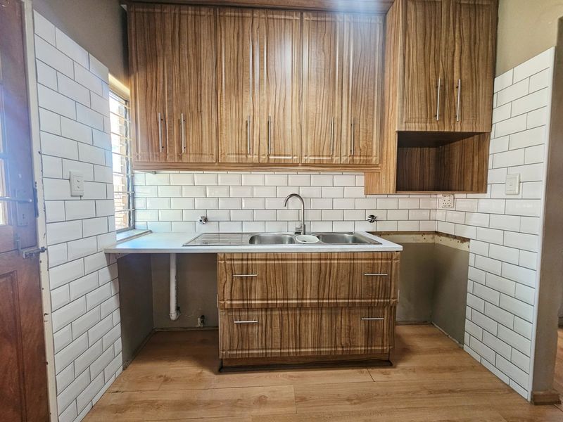 A kitchen area featuring wood-look cabinetry and white subway tile backsplash, currently requiring completion of base cabinetry and plumbing fixtures.