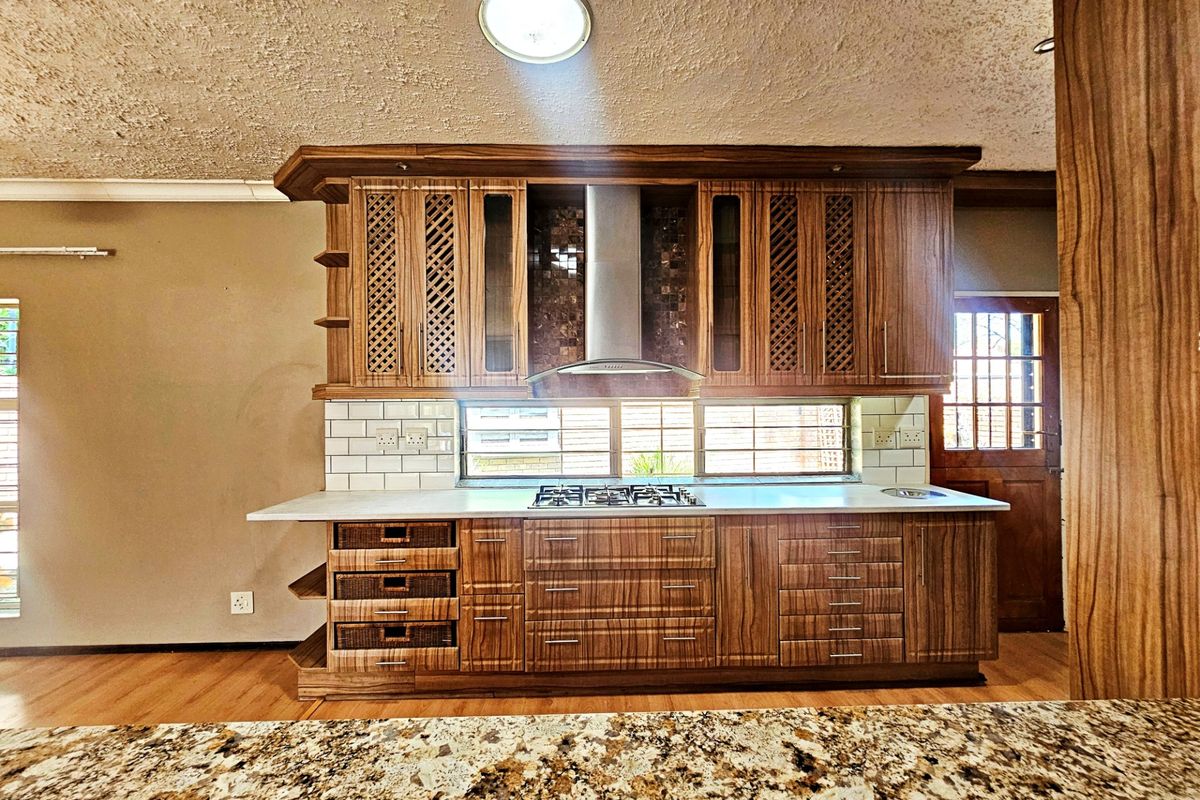 A well-maintained kitchen featuring custom wooden cabinetry, a gas hob with extractor fan, granite countertops, and a classic subway tile backsplash.