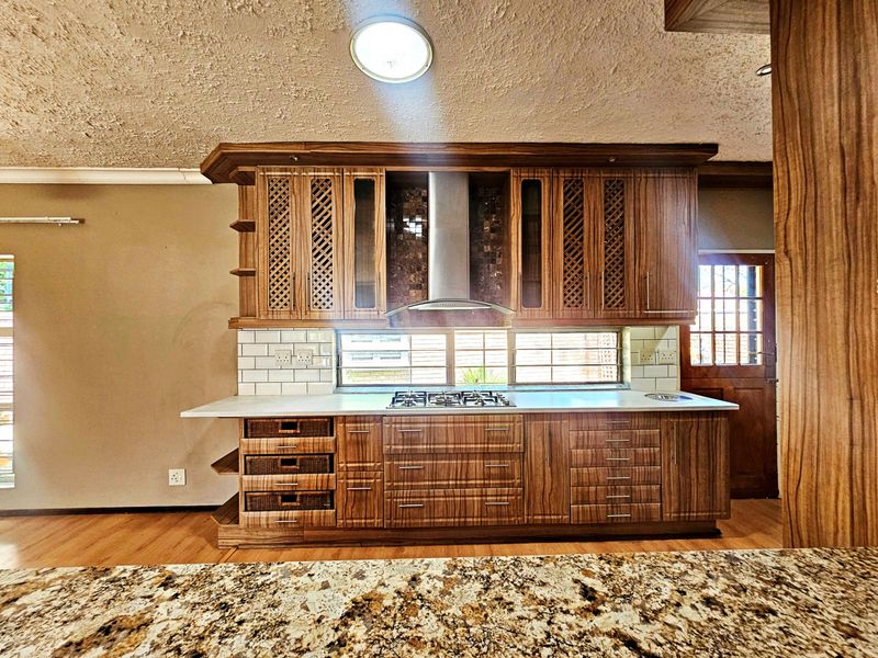 A well-maintained kitchen featuring custom wooden cabinetry, a gas hob with extractor fan, granite countertops, and a classic subway tile backsplash.