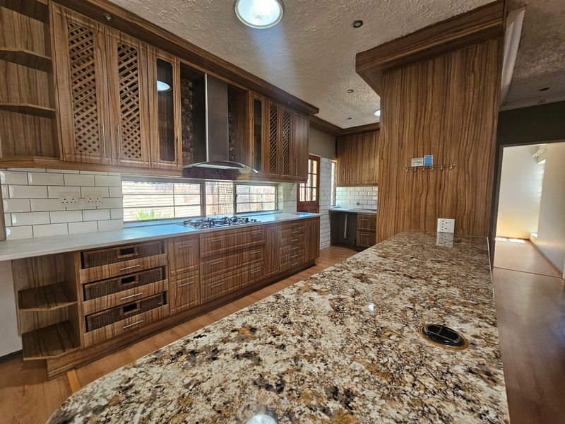 Spacious kitchen featuring extensive wood cabinetry, granite countertops, a gas hob, and a modern subway tile backsplash with integrated lighting.