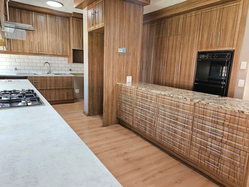 Spacious kitchen featuring extensive wood-grain cabinetry, granite countertops, built-in oven, gas hob, and a modern subway tile backsplash.