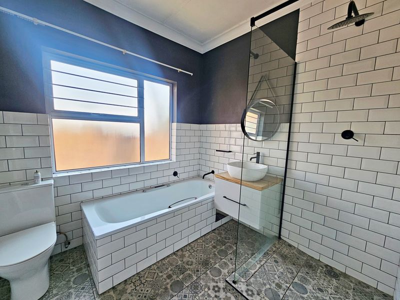 Modern bathroom featuring a built-in bathtub, wall-mounted vanity with vessel sink, glass shower screen, and stylish subway and patterned tile finishes.