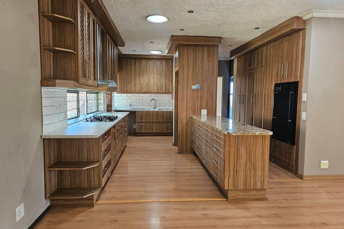 Spacious kitchen featuring extensive wood-grain cabinetry, granite countertops, built-in oven, gas hob, and a clean subway tile backsplash.