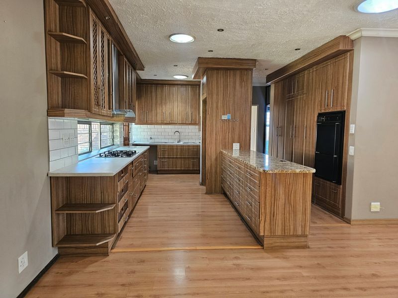 Spacious kitchen featuring extensive wood-grain cabinetry, granite countertops, built-in oven, gas hob, and a clean subway tile backsplash.