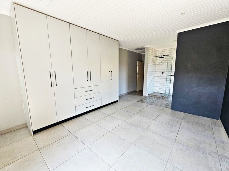Spacious bedroom featuring extensive built-in cabinetry, neutral tiled flooring, and an open-plan en-suite shower area with modern subway tiling.