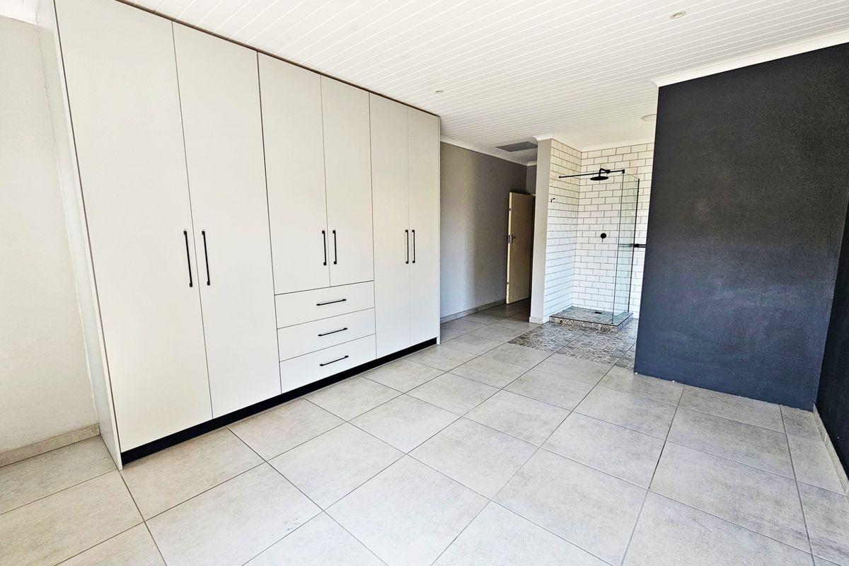 Spacious bedroom featuring extensive built-in cabinetry, neutral tiled flooring, and an open-plan en-suite shower area with modern subway tiling.