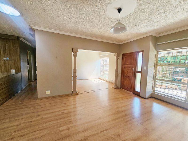 Spacious living area featuring laminate flooring, decorative columns, a timber entrance door, and a skylight, offering a bright and open layout.