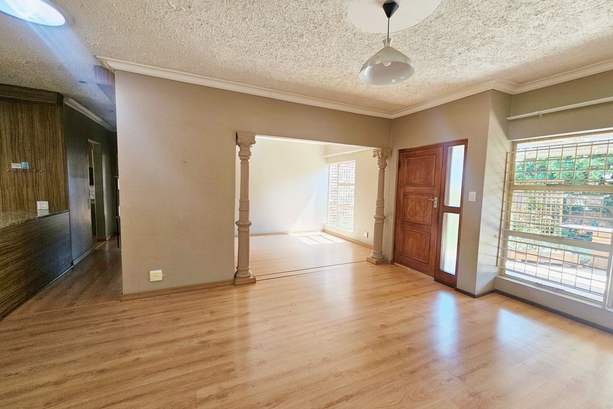 Spacious living area featuring laminate flooring, decorative columns, a timber entrance door, and a skylight, offering a bright and open layout.