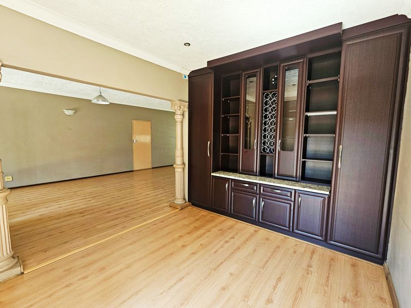 Spacious living area featuring built-in dark wood cabinetry, laminate flooring, and decorative columns, offering a versatile layout for interior design.