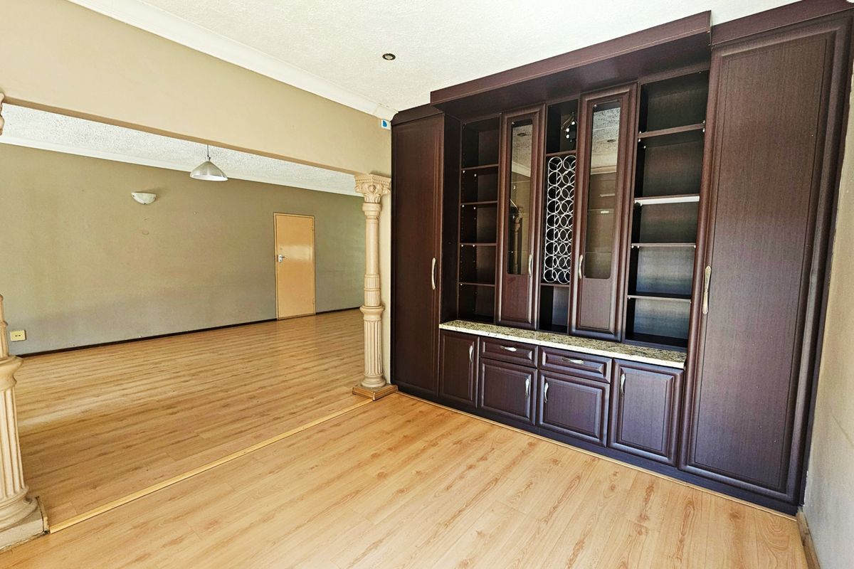 Spacious living area featuring built-in dark wood cabinetry, laminate flooring, and decorative columns, offering a versatile layout for interior design.