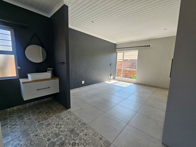 A spacious bedroom featuring a modern floating vanity with a vessel sink, tiled flooring, and a clean, contemporary aesthetic.
