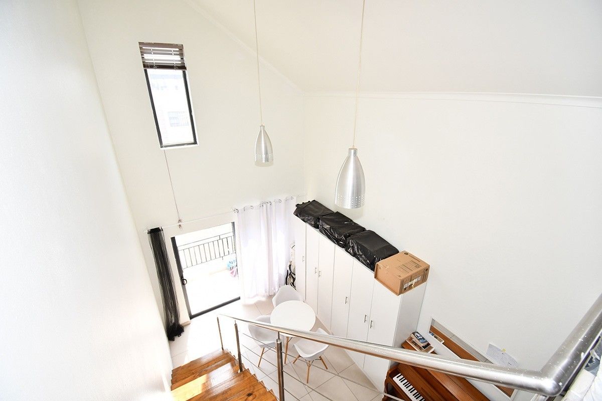 Bright living area featuring a vaulted ceiling, tiled floors, and a wooden staircase with a modern stainless steel handrail leading to a balcony.