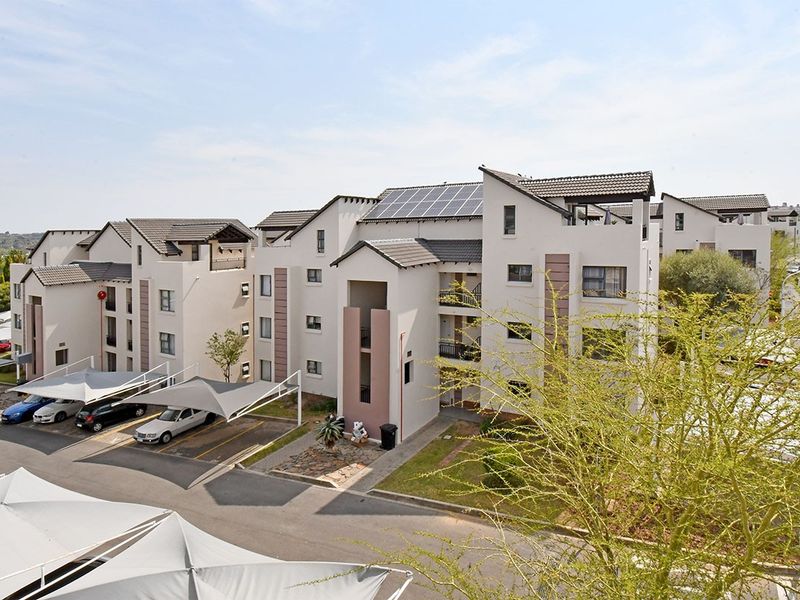 An elevated view of a modern apartment complex featuring multi-story buildings with tiled roofs, solar panels, and covered parking bays.