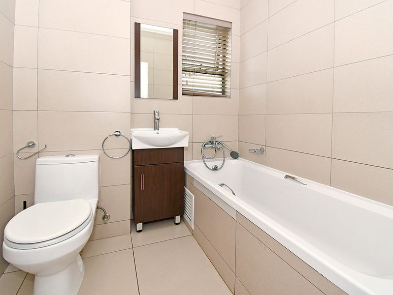 A clean, modern bathroom featuring neutral wall and floor tiles, a built-in bathtub, a vanity basin, and a toilet.
