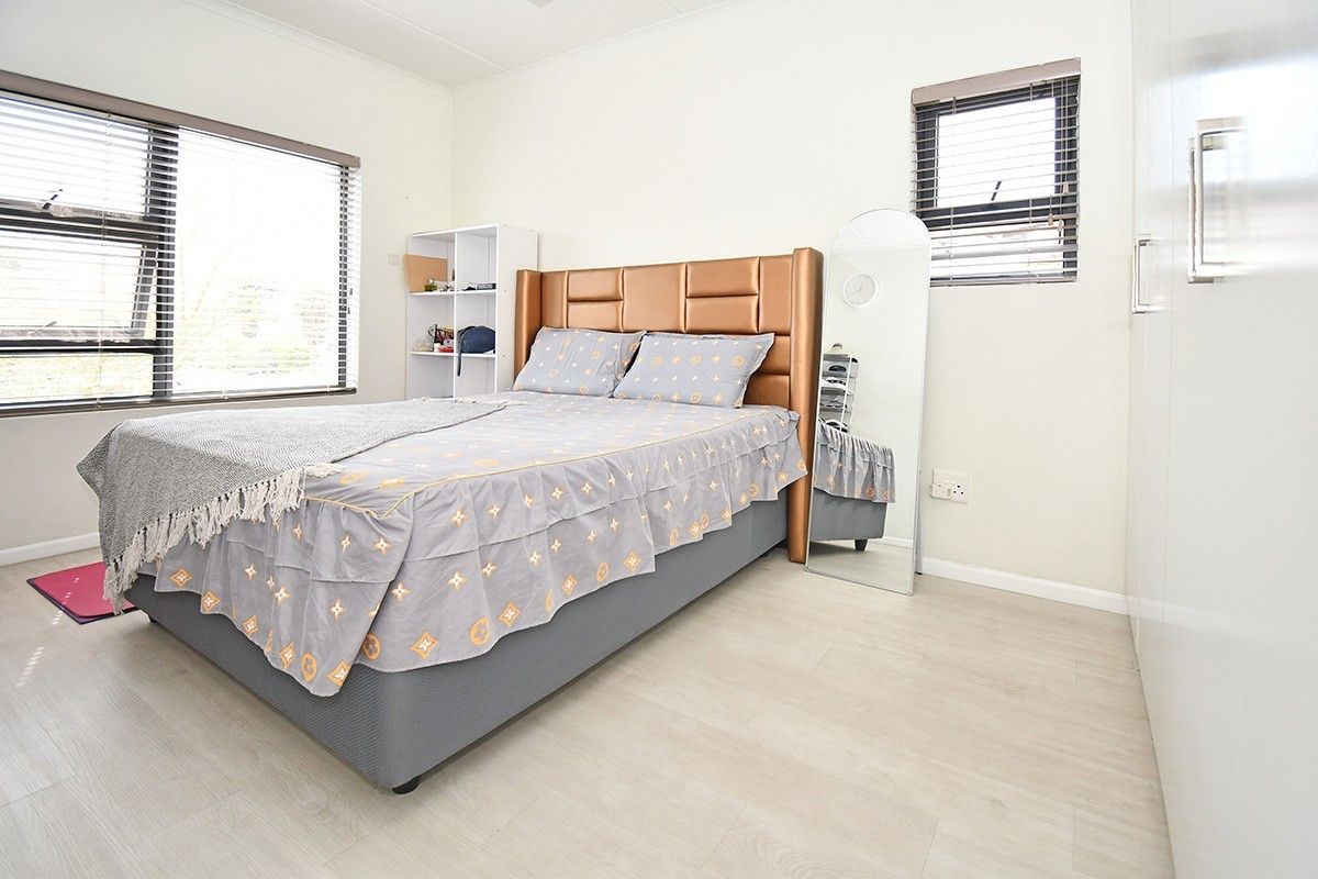 A bright bedroom featuring light-toned laminate flooring, built-in cupboards, and venetian blinds on the windows.