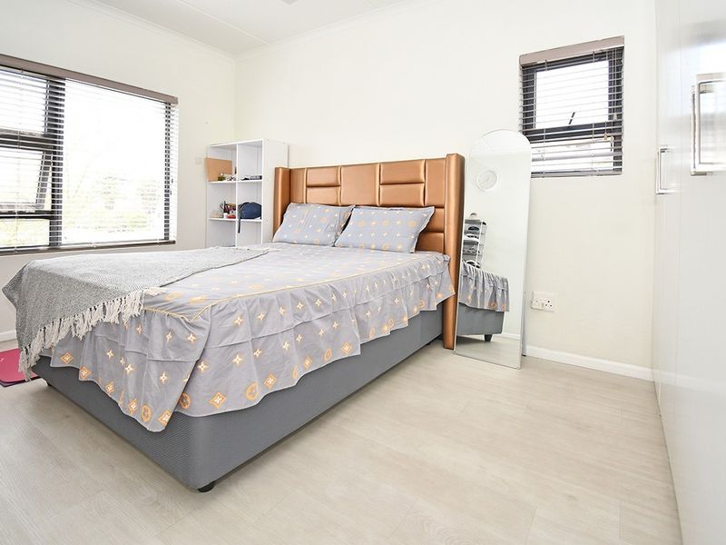 A bright bedroom featuring light-toned laminate flooring, built-in cupboards, and venetian blinds on the windows.