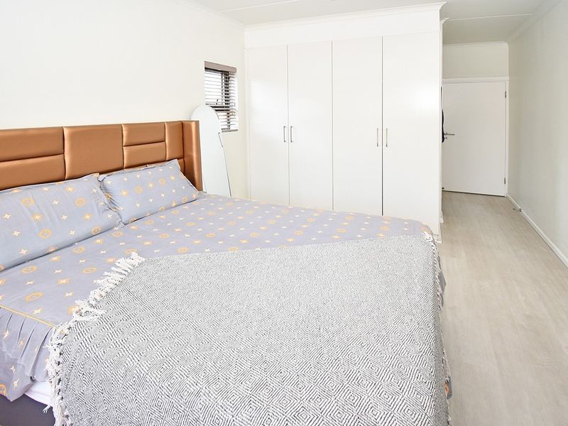 A well-maintained bedroom featuring light laminate flooring, neutral walls, and ample built-in cupboard storage.