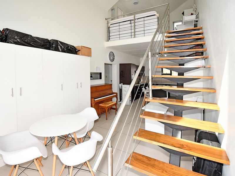 Open plan living area featuring a mezzanine level, modern timber staircase with stainless steel balustrade, and built-in storage cabinetry.