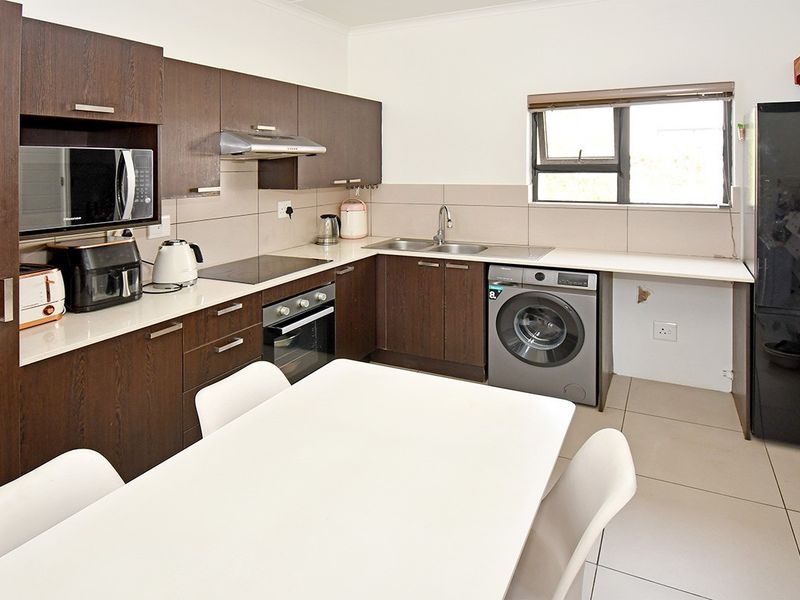 A functional kitchen featuring dark wood cabinetry, built-in appliances, tiled splashbacks, and dedicated space for laundry equipment.