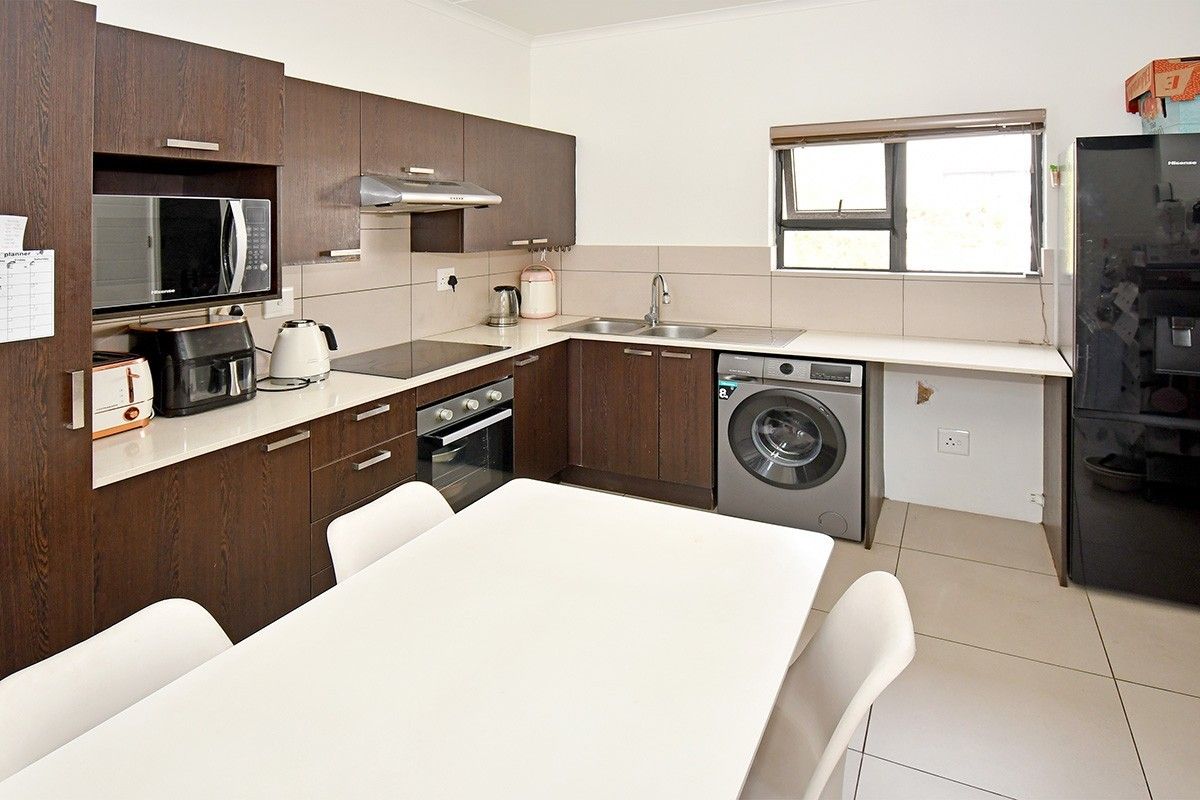 A functional kitchen featuring dark wood cabinetry, built-in appliances, tiled splashbacks, and dedicated space for laundry equipment.
