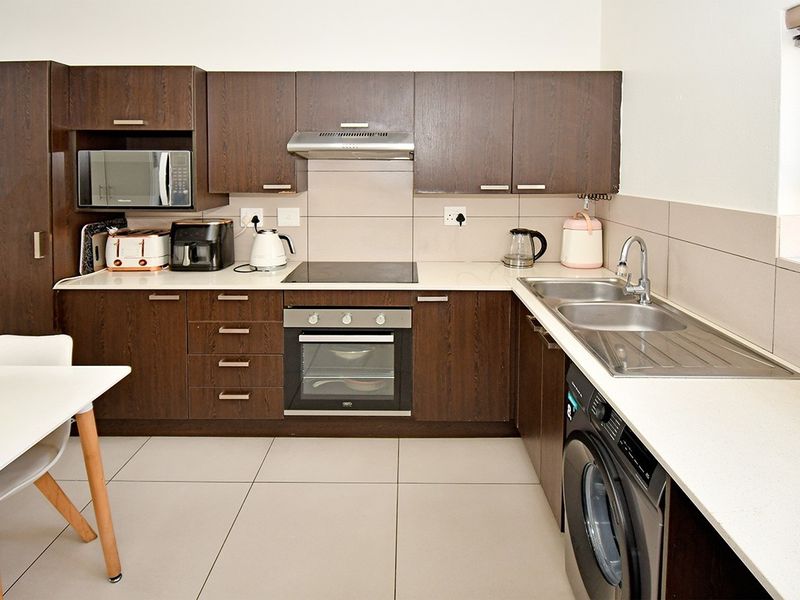 A functional kitchen featuring dark wood cabinetry, built-in oven, electric hob, extractor fan, and a double stainless steel sink with tiled splashbacks.