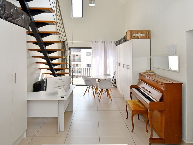 Open-plan living area featuring high ceilings, tiled flooring, a modern metal staircase, and direct access to a balcony.