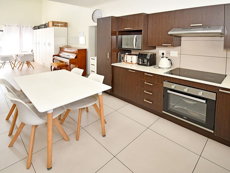 Open-plan kitchen and dining area featuring dark wood cabinetry, integrated appliances, and neutral tiled flooring throughout the living space.