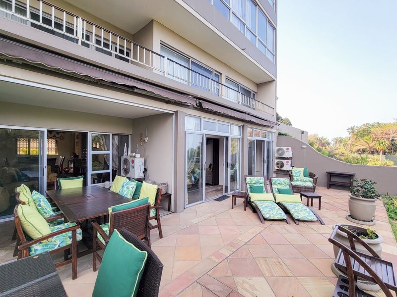 Spacious outdoor patio area featuring tiled flooring, retractable awnings, and direct access to the apartment interior through multiple sliding glass doors.