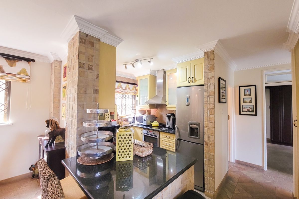 A functional kitchen featuring granite countertops, built-in cabinetry, and stone-clad pillars, offering a practical layout with integrated appliances and classic crown molding details.
