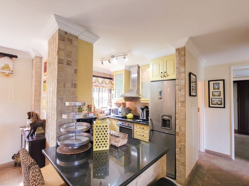 A functional kitchen featuring granite countertops, built-in cabinetry, and stone-clad pillars, offering a practical layout with integrated appliances and classic crown molding details.