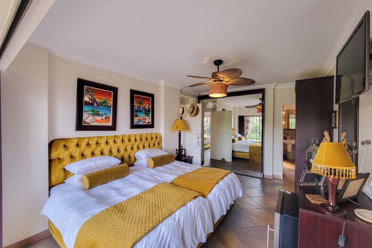 A well-maintained bedroom featuring tiled flooring, crown molding, a ceiling fan, and large mirrored wardrobe doors providing access to an en-suite bathroom.