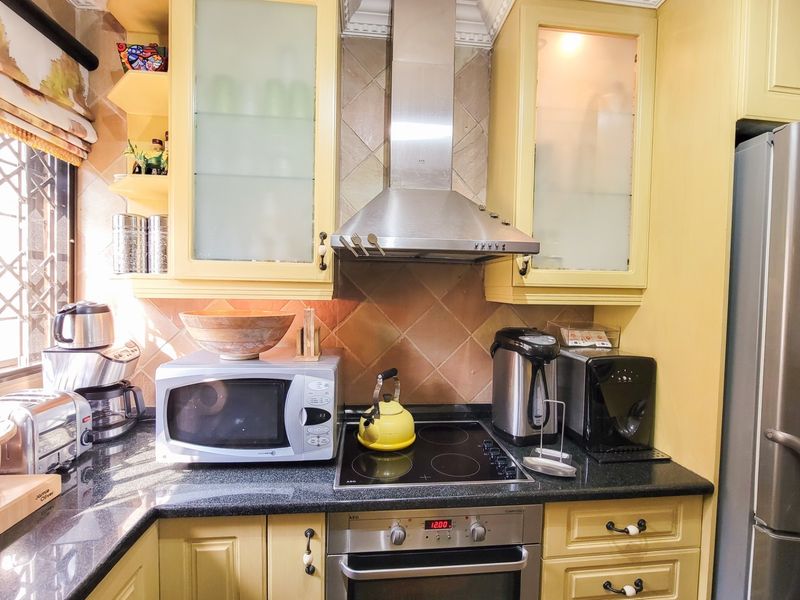 A functional kitchen featuring yellow cabinetry, granite countertops, a tiled backsplash, and integrated stainless steel appliances including an oven and extractor fan.