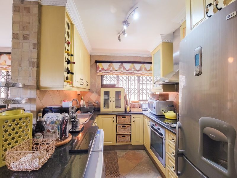 A compact, U-shaped kitchen featuring yellow cabinetry, granite countertops, built-in oven, extractor fan, and tiled finishes with a security-gated window.