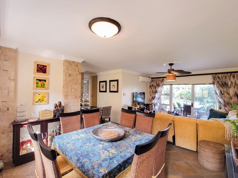 Open-plan living and dining area featuring tiled floors, a stone feature wall, ceiling fan, and sliding glass doors leading to an outdoor patio.