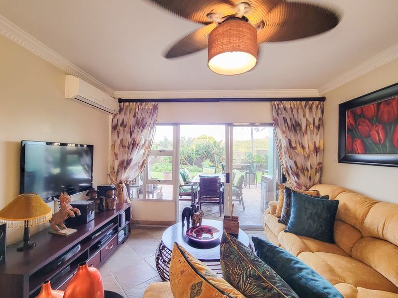 A comfortable living room featuring tiled flooring, crown molding, a ceiling fan, and a split-system air conditioner, with direct access to an outdoor patio.