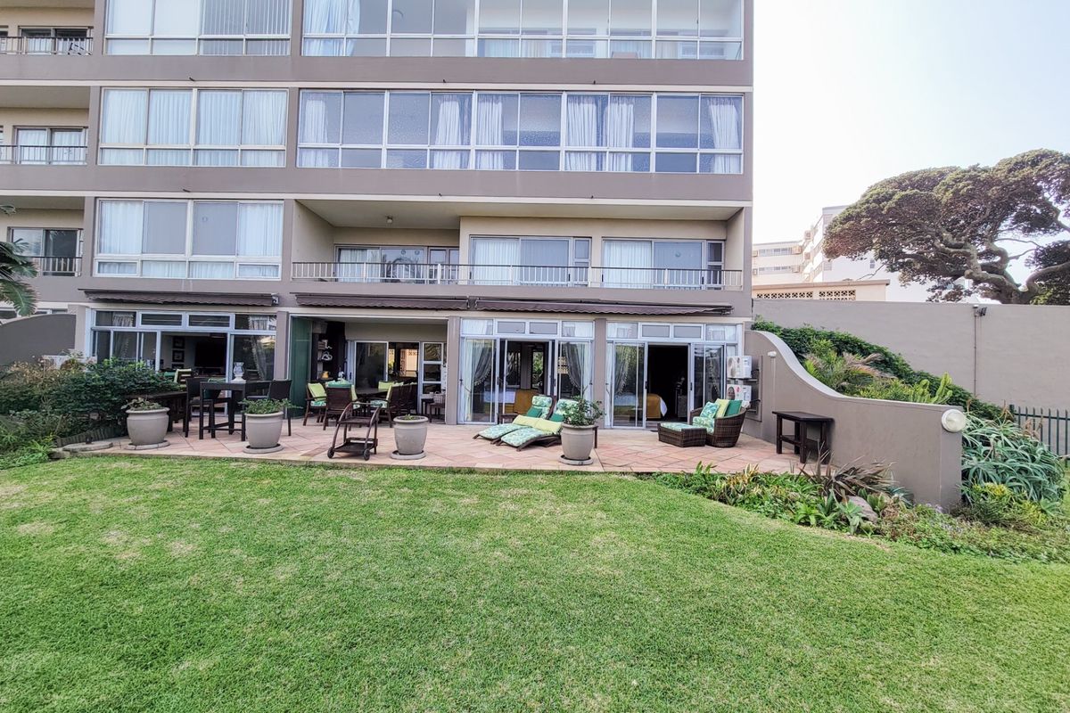Rear view of the apartment building featuring a spacious tiled patio, landscaped garden, and multiple sliding glass doors providing access to the interior.