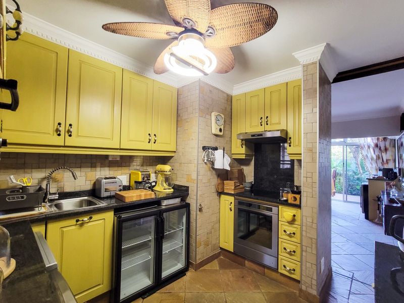 A compact kitchen featuring yellow cabinetry, granite countertops, built-in oven, extractor fan, and an integrated undercounter fridge with tiled finishes.