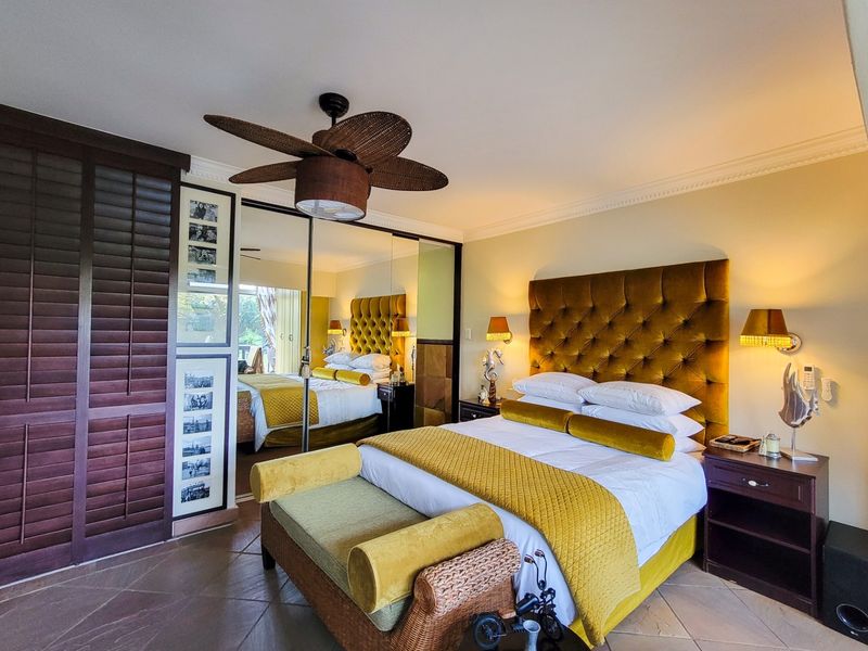 A well-maintained bedroom featuring tiled flooring, crown molding, a ceiling fan, and large mirrored built-in cupboards providing ample storage space.