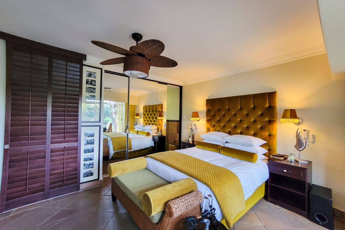 A well-maintained bedroom featuring tiled flooring, crown molding, a ceiling fan, and large mirrored built-in cupboards providing ample storage space.