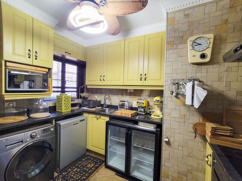 A compact, well-equipped kitchen featuring yellow cabinetry, granite countertops, a tiled backsplash, and integrated appliances, including a washing machine and under-counter fridge.