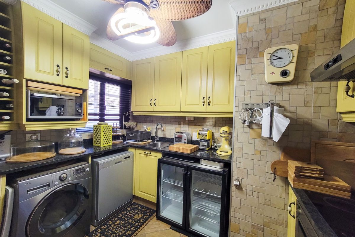 A compact, well-equipped kitchen featuring yellow cabinetry, granite countertops, a tiled backsplash, and integrated appliances, including a washing machine and under-counter fridge.