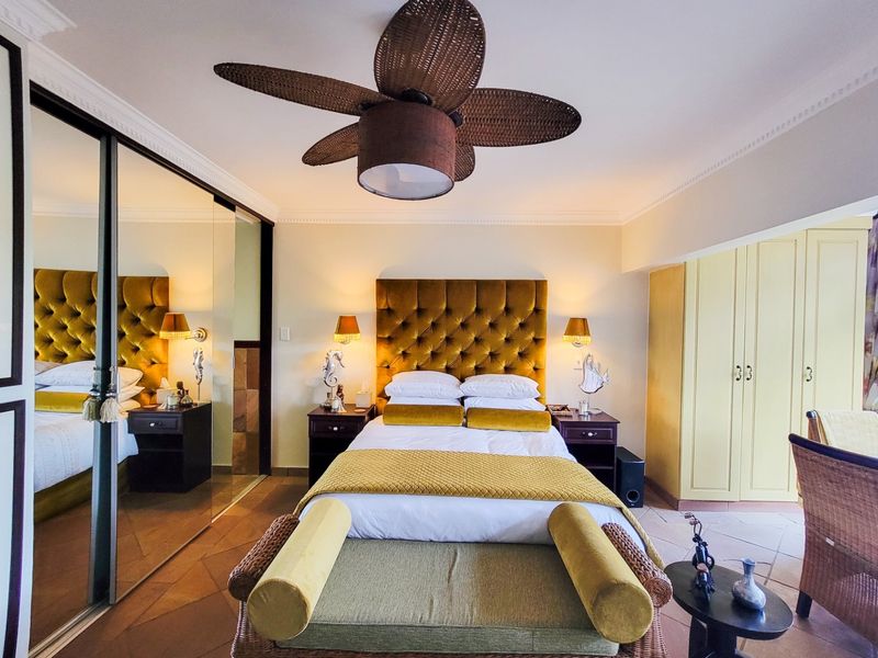 A well-maintained bedroom featuring tiled flooring, crown molding, a ceiling fan, and extensive mirrored built-in wardrobe storage.