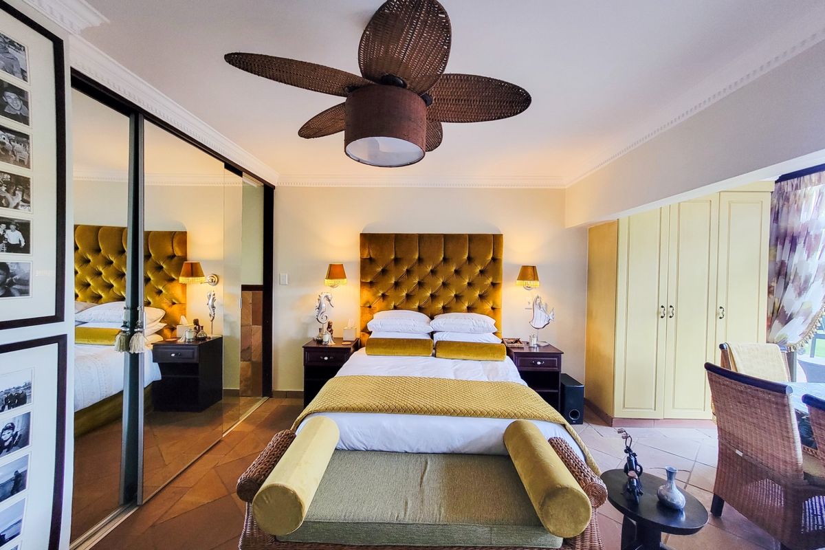 A well-maintained bedroom featuring tiled flooring, crown molding, a ceiling fan, and extensive mirrored built-in wardrobe storage.
