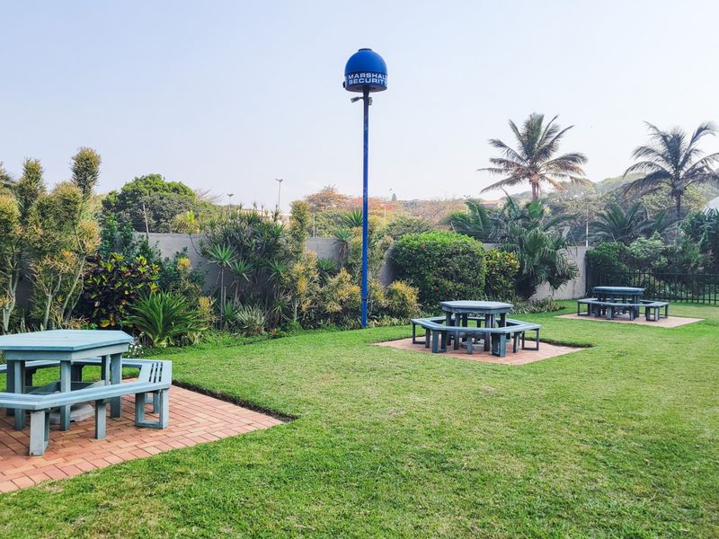 A well-maintained garden area featuring paved seating sections, lush landscaping, and a security camera pole.