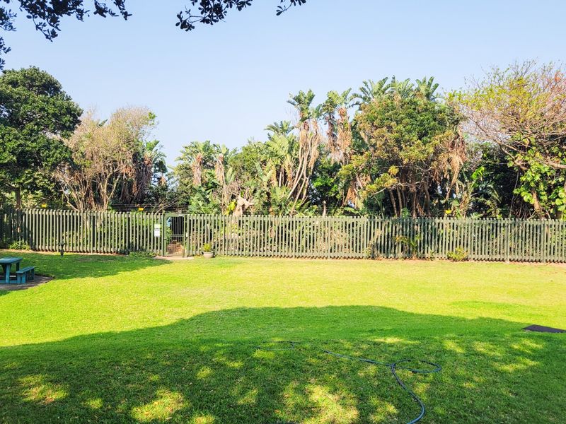 A well-maintained private garden featuring a lush lawn, mature trees, and secure perimeter fencing with an integrated pedestrian gate.