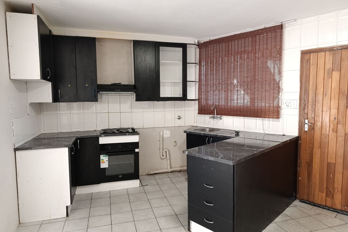A functional kitchen featuring dark cabinetry, laminate countertops, built-in oven, and hob, with tiled flooring and backsplash. Requires minor finishing and maintenance.